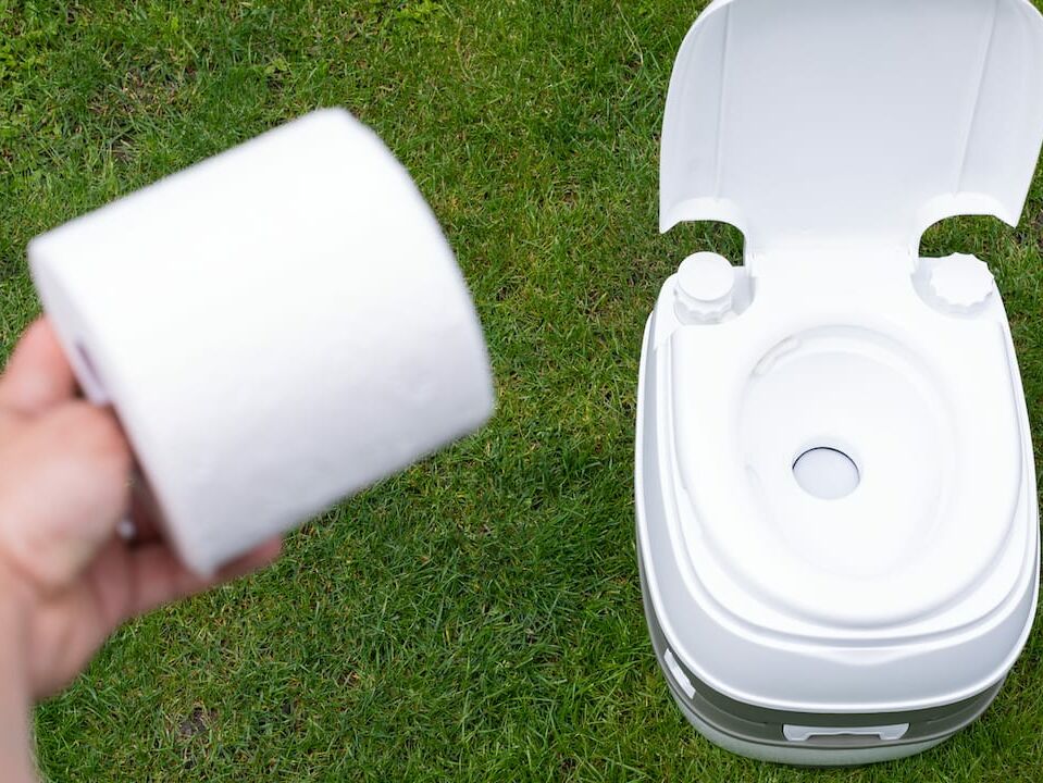 Eine Campingtoilette die aufgeklappt auf einer Wiese steht 