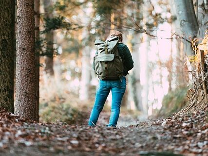 Eine Frau die mit einem Rucksack auf dem Rücken auf einem Waldweg steht und sich verlaufen hat.